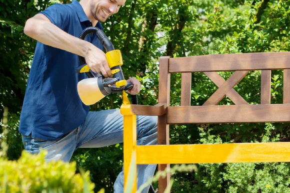 Person lackiert Gartenbank gelb